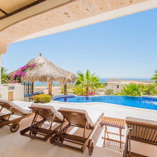 Covered patio lounge chairs and pool with ocean view
