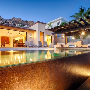 Stunning infinity pool with illuminated water feature reflects the villa's elegant architecture under evening skies, creating your perfect backdrop for mountain-view relaxation.