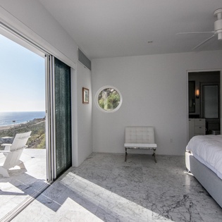 Wake up to stunning ocean views in this serene bedroom where marble floors and a ceiling fan create perfect comfort for your coastal escape.