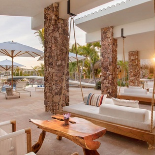 A stunning waterfront setting where you can lounge on hanging swings or relax under umbrellas, surrounded by palm trees and sunset views over the bay.