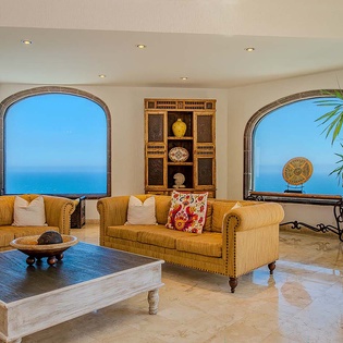 Unwind in your elegant living room where arched windows frame breathtaking ocean vistas. Sink into plush seating and let the serene blue horizon become your daily backdrop.