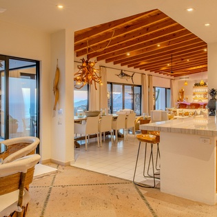 Your spacious open-plan kitchen flows seamlessly into dining and living areas, where warm wood beams and ocean views create the perfect gathering space.