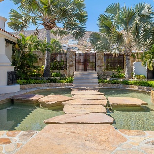 Stone-paved entrance courtyard with palms and shallow pools guides guests toward the tropical, mountain-backed retreat—a calming first impression of the property's coastal serenity.