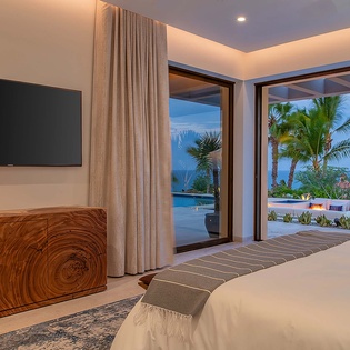 Drift off with floor-to-ceiling glass framing your private tropical oasis—swaying palms, shimmering pool, and evening sky just beyond your bed.