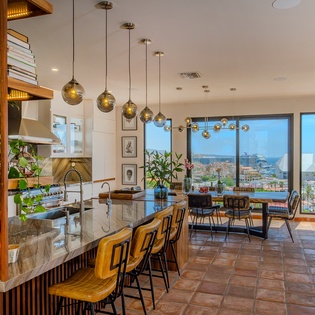 Imagine sipping morning coffee at this sleek kitchen island, sunlight streaming through floor-to-ceiling windows that frame breathtaking ocean views. Warm pendant lights, lush greenery, and open shelving create a space where you'll love gathering.