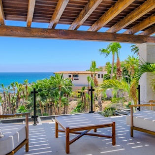 Your private terrace offers stunning ocean views framed by swaying palms, where comfortable seating invites peaceful moments under tropical shade.