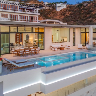 Modern luxury villa with stunning hillside architecture featuring floor-to-ceiling windows and an infinity pool overlooking the Mediterranean landscape.