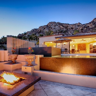 Stunning desert hillside retreat featuring a glowing firepit, infinity pool, and open-air terrace where you can unwind under a clear evening sky surrounded by dramatic rocky peaks.