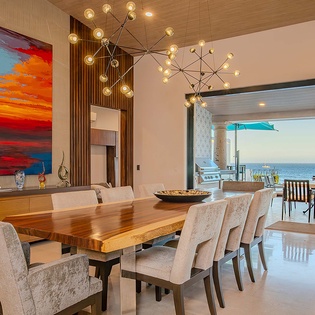 Gather around this stunning wood table beneath designer lighting while ocean breezes and sea views flow through open doors—your dream vacation dining experience awaits.