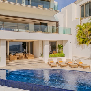 Modern beachfront villa featuring a pristine swimming pool, tropical landscaping, and seamless indoor-outdoor living spaces.