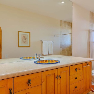 Step into your private oasis with dual handcrafted sinks, warm travertine finishes, and a rain shower enclosure inviting you to unwind after a day in paradise.