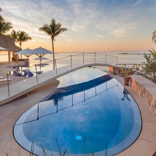 Beachfront infinity pool framed by swaying palms meets tropical ocean views—a stunning backdrop to unwind as the sun dips over the horizon.