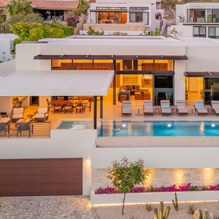 Stunning modern villa showcases contemporary design with terraced levels, infinity pool, and warm evening lighting in an upscale hillside neighborhood.