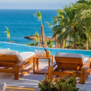 Luxurious infinity pool area with premium teak loungers overlooking pristine tropical waters and swaying palms.