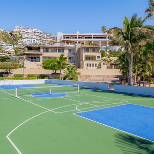 Multi-sport court featuring tennis and basketball facilities set against a stunning hillside backdrop with palm trees and luxury homes.