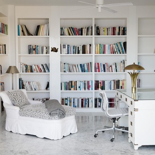 Curl up with your favorite book in this bright library featuring floor-to-ceiling shelves and a cozy reading chair.