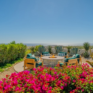 Vibrant bougainvillea frames this stunning rooftop terrace where comfortable seating surrounds a circular fire pit, creating the perfect spot for evening gatherings.
