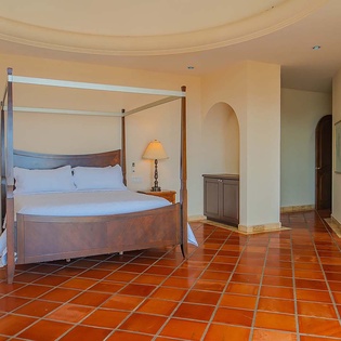 Drift off in this elegant four-poster bed with crisp white linens, framed by warm terracotta tiles and soft lighting for your ultimate retreat.