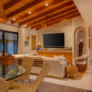 Relax in your stunning living room featuring exposed wood beams, modern entertainment center, and elegant wicker furnishings that create the perfect blend of rustic charm and contemporary comfort.