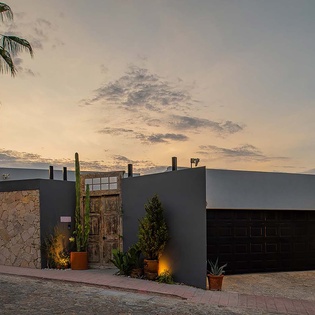 Modern desert retreat featuring contemporary architecture with stone accents, native landscaping, and warm ambient lighting against a peaceful evening sky.