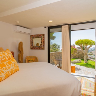 Wake up to stunning garden views from your bright, airy bedroom featuring warm orange accents and natural wicker touches.