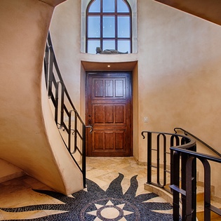 Step into a uniquely designed entryway where warm adobe curves and a striking mosaic sunburst floor greet you. The arched window above floods this inviting space with natural light, setting the tone for your stay.