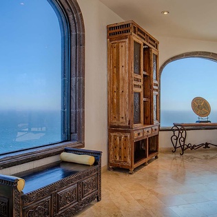 This elegant space frames sweeping ocean views through dramatic arched windows, where handcrafted wood furnishings and warm tiles create an inviting retreat to unwind and watch the waves.