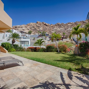 A hillside vacation resort community with multiple buildings nestled against rugged terrain, surrounded by manicured lawns, palm trees, and vibrant tropical landscaping under clear blue skies.