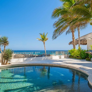 Private oceanfront pool surrounded by swaying palms and tropical décor, where crystal-clear water meets stunning sea views under endless blue skies.