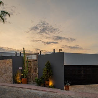 Modern desert property exterior with sleek architectural lines, stone accents, and desert landscaping welcomes guests at twilight.