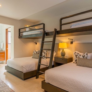 Settle into your stylish sleeping space where custom bunk beds and a plush lower bed create the perfect retreat for family or friends, all bathed in warm, welcoming light.