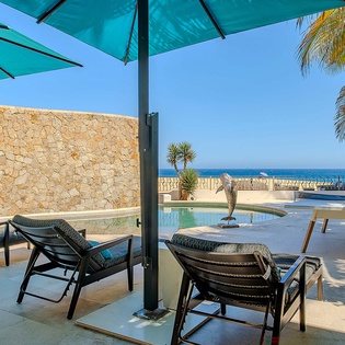 Lounge under turquoise umbrellas by your private pool, where palm trees frame stunning sea views and sunshine warms your oceanfront terrace.