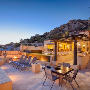 Hillside retreat featuring expansive terrace, poolside loungers, and dramatic mountain views as twilight settles over the surrounding coastal community.