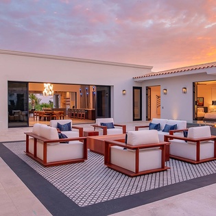 Stunning sunset hues paint the sky above this inviting outdoor lounge, where you'll find plush seating arranged around a contemporary fire feature—perfect for evening conversations under the stars.