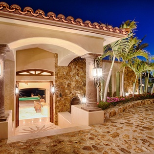 Mediterranean-style villa entrance with archways, stone columns, and lush tropical landscaping welcomes arrivals at twilight.