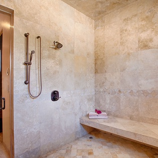 Step into your spa-inspired walk-in shower featuring dual showerheads, luxurious travertine walls, and a built-in bench where you can relax and unwind after exploring the area.