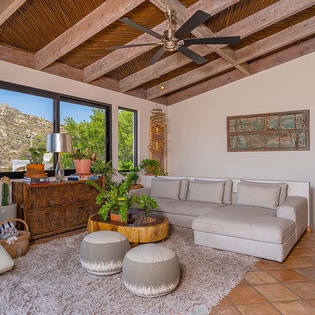 Settle into your serene living room with soaring wood beam ceilings, plush seating, and mountain views framing peaceful moments of your desert retreat.