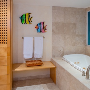 Unwind in your spa-like bathroom featuring a luxurious jetted tub, tropical fish artwork, and warm wood storage for ultimate relaxation.
