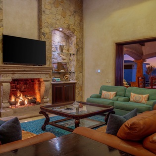 Unwind in your elegant living room where crackling fireplace warmth meets stunning sunset views through expansive doors.