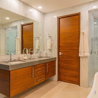 Step into this spa-inspired bathroom, where marble walls and warm wood tones create a serene escape. Dual sinks and a glass-enclosed shower invite you to unwind in style.