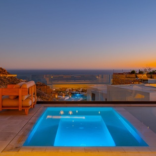 Modern villa with illuminated pool overlooking the sea during golden hour sunset.