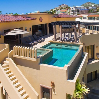 A luxurious hillside villa featuring a private rooftop pool with lounge chairs and shaded cabana, set against scenic neighborhood views and clear blue skies.