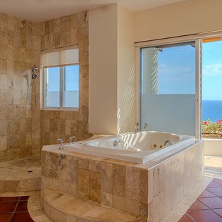 Soak in your spa tub while gazing at the sparkling sea through the glass doors. Warm tile and travertine accents give this bathroom an inviting, resort-like feel.