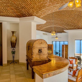 The stunning brick-vaulted ceiling draws your eye across this unique space where rustic wooden furnishings blend with coastal views through floor-to-ceiling windows, creating your perfect seaside retreat.