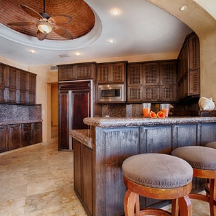 Whip up your favorite meals in this spacious kitchen, featuring dark wood cabinetry, granite countertops, modern appliances, and a breakfast bar with inviting seating. The tropical ceiling fan adds a breezy touch.