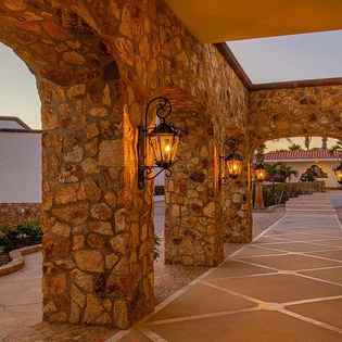 Stone archways frame a welcoming pathway, glowing with warm lanterns as the evening sky sets the scene for your arrival.