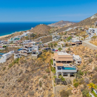 Stunning aerial view of coastal hillside community with beachfront access and mountain backdrop in sunny Mediterranean setting.