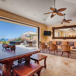 Your living space opens seamlessly onto a private terrace with ocean views, blending comfort and coastal elegance with rich wood accents and tropical ceiling fans overhead.