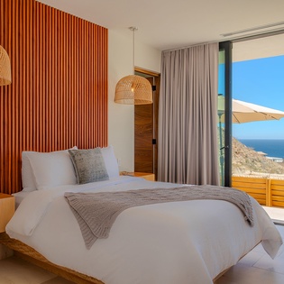 Wake to stunning ocean views from your luxurious bed, with warm wood accents and woven pendant lights creating a serene coastal retreat.