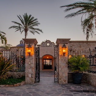 Grand stone entrance with ornate ironwork gates and glowing lanterns creates an elegant arrival experience surrounded by tropical palms.